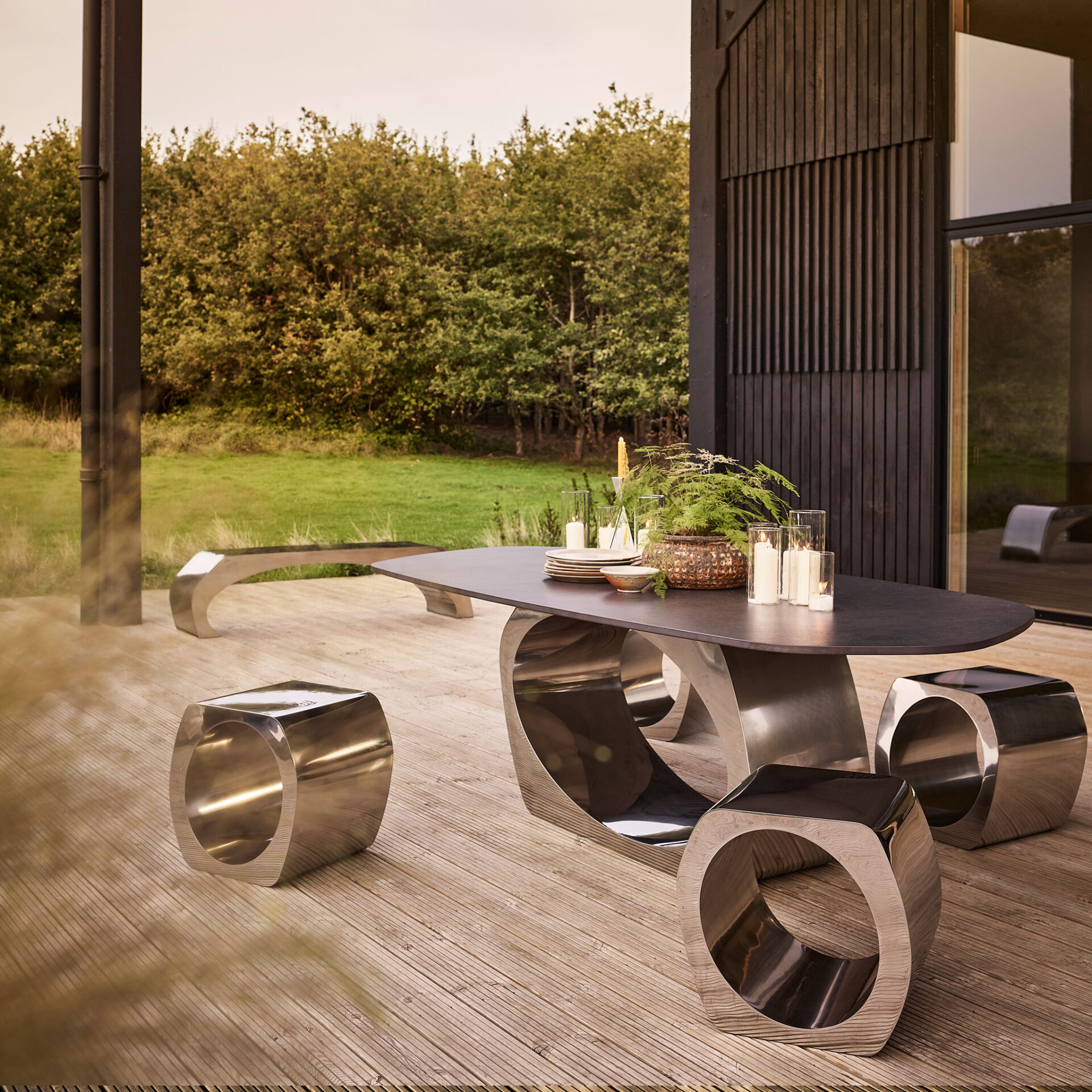 Skye dining table with a black stone top and Skye stools in polished stainless steel, for outdoors